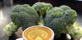 A broccoli latte surrounded by bunches of raw broccoli