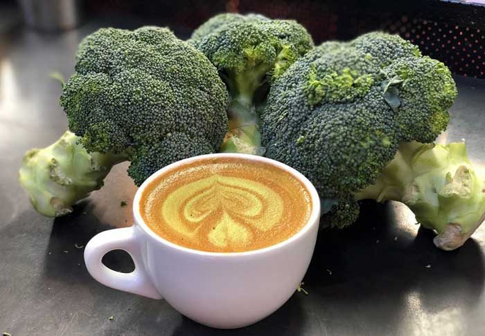 A broccoli latte surrounded by bunches of raw broccoli