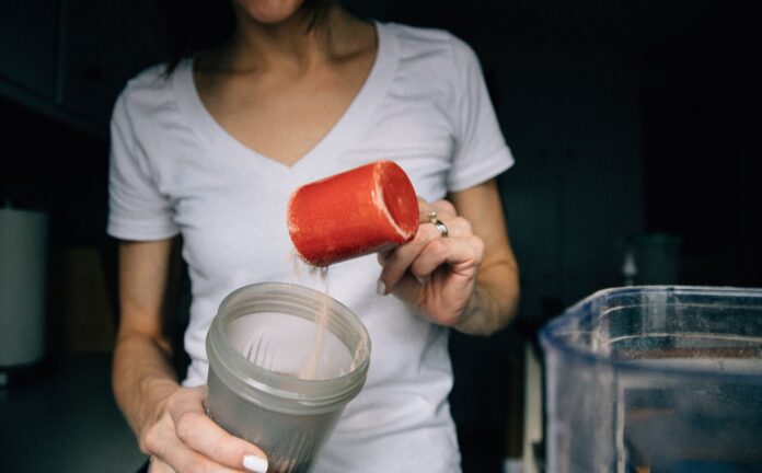 a woman adding a scoop of protein powder