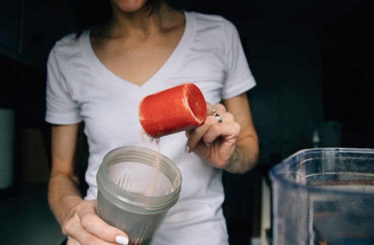 a woman adding a scoop of protein powder